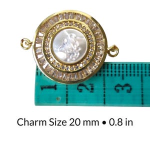 May include: Gold-toned round charm with a central white cameo design, surrounded by clear baguette-cut stones. The charm measures 0.8 inches (20 mm) in diameter and has two small loops for attachment. The text "Charm Size 20 mm &bull; 0.8 in" is below the charm.