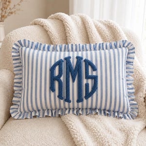 May include: A rectangular throw cushion featuring a blue and white vertical striped pattern with a ruffled edge. The centre of the cushion displays a large, dark blue embroidered monogram with the letters RMS in a textured, raised stitch style.