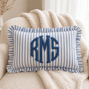 May include: A rectangular throw pillow featuring a blue and white vertical striped pattern with a ruffled edge. The center of the pillow displays a large, textured, dark blue embroidered monogram with the letters RMS in a classic serif font.