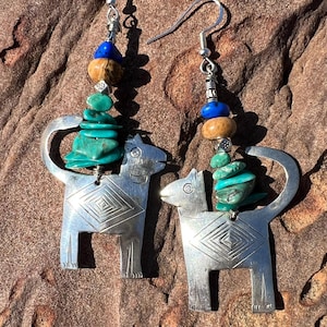 May include: A pair of silver earrings featuring a stylised dog design with turquoise and brown beads. The earrings are hanging from silver hooks.