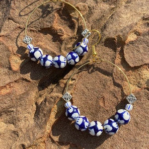 May include: A pair of gold hoop earrings with blue and white patterned ceramic beads. The beads have a white background with blue floral designs.