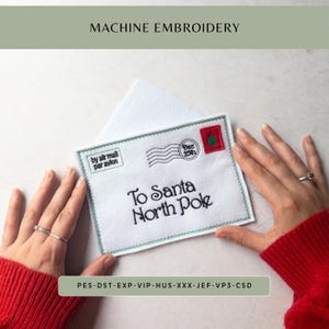 May include: A white felt envelope with machine embroidery featuring the text To Santa North Pole, a postmark reading Dec 25th, a red stamp with a green tree, and the text by air mail par avion, finished with a green stitched border.