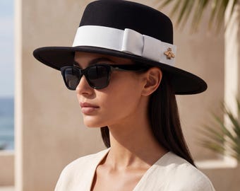 May include: A black fedora hat with a white band and a gold bee emblem. The hat is paired with black sunglasses. The hat has a wide brim and a structured crown. The hat is a stylish accessory.