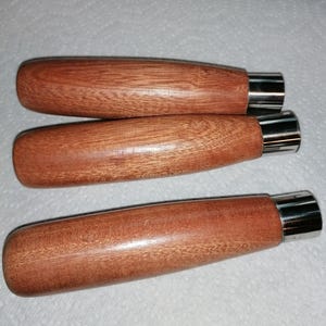 May include: Three reddish-brown wooden handles with a polished finish. Each handle features a cylindrical, stainless steel ferrule at one end. The handles are arranged in a row, possibly for a set of tools or equipment.
