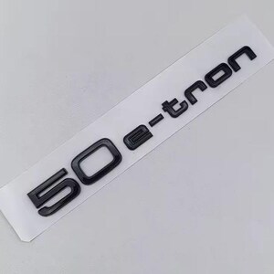May include: Black 50 e-tron emblem on a white backing. The emblem features a glossy finish and is designed for automotive applications. The text is in a bold, sans-serif font.