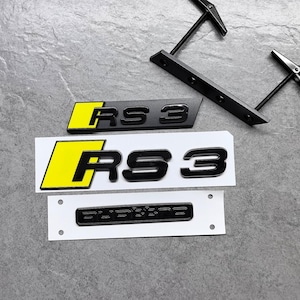 May include: Black and yellow RS3 car emblem with a black Quattro emblem on a white backing. The RS3 emblem has a yellow background with black lettering. Also included are black tools.