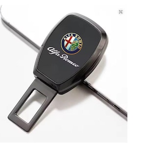 Puede incluir: Hebilla de cinturón de seguridad negra con el logotipo de Alfa Romeo en el centro. El logotipo es un emblema circular con una cruz roja y una serpiente verde. Las palabras "Alfa Romeo" están escritas en blanco.