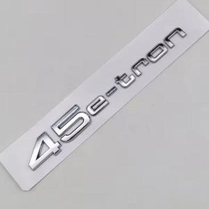 May include: A silver-colored emblem with the text "45 e-tron" on a white rectangular background. The numbers and letters are in a bold, sans-serif font, with a metallic sheen. The emblem is likely for a vehicle.