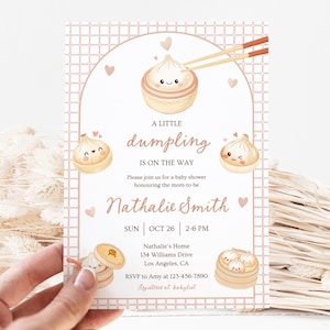 Könnte beinhalten: Eine Babyparty-Einladung mit einem Knödel-Thema. Die Einladung zeigt Illustrationen von lächelnden Knödeln, Essstäbchen und Herzen. Der Text lautet "A Little Dumpling is on the Way" und enthält die Veranstaltungsdetails und den Namen der werdenden Mutter.