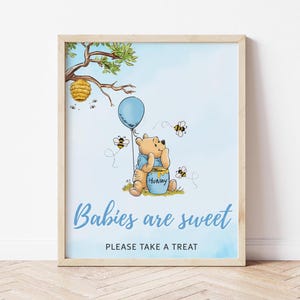 Könnte beinhalten: Ein gerahmter Druck mit einem Cartoon-Bären, einem Honigtopf und einem blauen Ballon. Das Bild zeigt einen Bienenstock, Bienen und den Text "Babies are sweet, PLEASE TAKE A TREAT" auf hellblauem Hintergrund. Der Rahmen ist hellbraun.