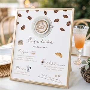 May include: A framed cafe menu with a gold border. The menu features watercolor illustrations of coffee beans, a latte, a croissant, and coffee-related icons. Text includes "Cafe bébé menu", coffee options, and add-ons.