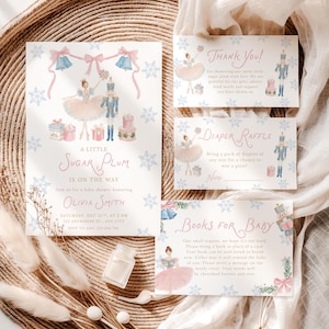 Könnte beinhalten: Ein Set aus Babyparty-Papeterie mit Aquarellillustrationen einer Ballerina und eines Nussknackers, umgeben von blauen Schneeflocken. Die Karten enthalten Texte wie A Little Sugar Plum Is On The Way, Thank You, Diaper Raffle und Books For Baby mit rosa und blauen Akzenten.
