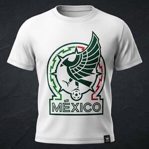 Pu&ograve; includere: Una t-shirt bianca a maniche corte con una grafica centrale raffigurante un'aquila stilizzata con le ali spiegate, un pallone da calcio e la scritta M&Eacute;XICO in verde scuro e rosso. Il design &egrave; circolare con accenti geometrici.