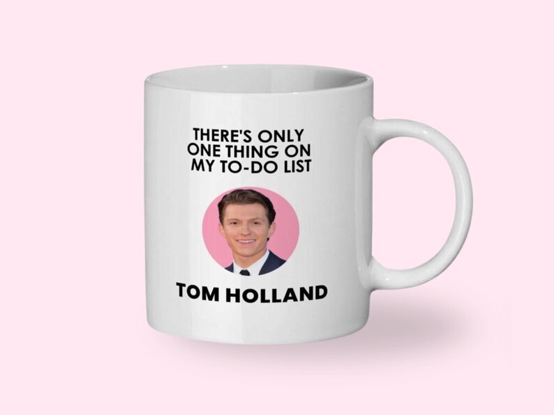 May include: White ceramic mug with a handle featuring the text "THERE'S ONLY ONE THING ON MY TO-DO LIST" above a photo of Tom Holland in a pink circle, with "TOM HOLLAND" printed below.