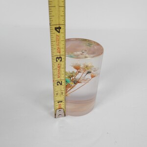 May include: A clear glass cylinder with a bouquet of dried white flowers and green leaves inside. The cylinder is approximately 3 inches tall.