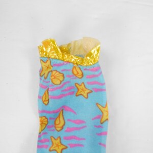 May include: A blue and pink fabric doll dress with a yellow trim and a seashell and starfish pattern.
