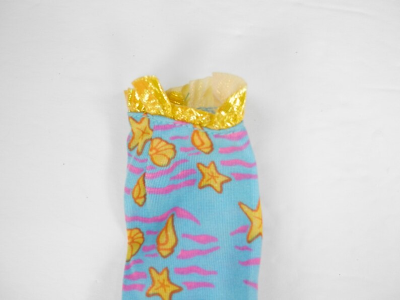 May include: A blue and pink fabric doll dress with a yellow trim and a seashell and starfish pattern.