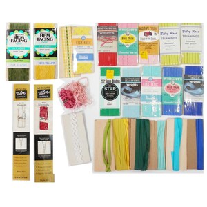 Könnte beinhalten: Eine Sammlung von Nähzubehör, darunter Schrägband, Rick Rack, Saumaufschlag, Reißverschlüsse und Nahtband. Die Artikel sind in verschiedenen Farben wie Gelb, Grün, Rot und Blau erhältlich. Das Bild enthält mehrere Packungen und Spulen mit Besatz.