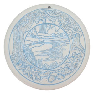 Puede incluir: Adorno redondo de cerámica blanca con un diseño azul grabado. El diseño presenta un paisaje con árboles, agua y dos patos. También se incluyen bellotas y follaje. Hay un pequeño agujero en la parte superior para colgar.