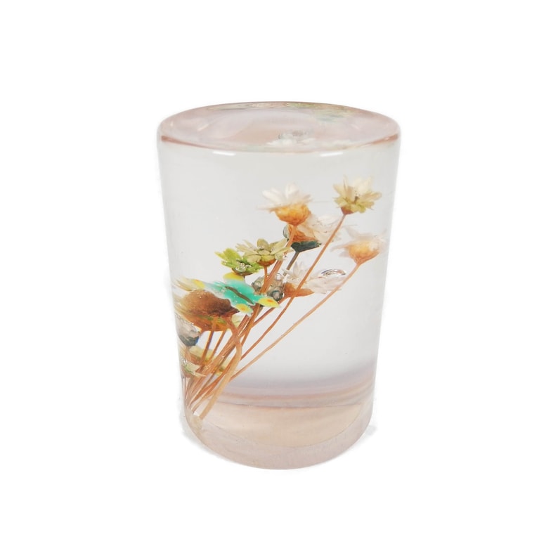 May include: A clear glass cylinder with a bouquet of dried flowers inside. The flowers are white, brown, and green.