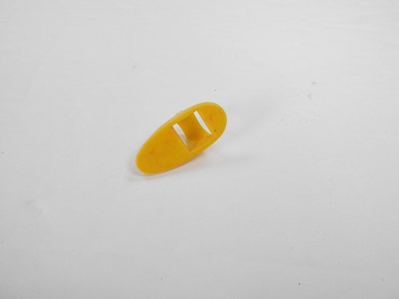 May include: A yellow plastic finger pick with a rectangular opening in the center.