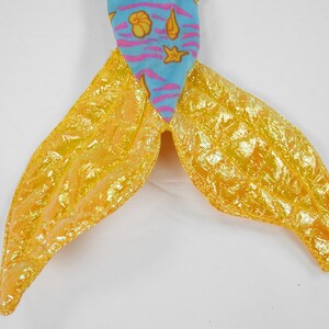 May include: A mermaid tail costume with a blue and pink fabric top and a yellow iridescent fabric bottom.