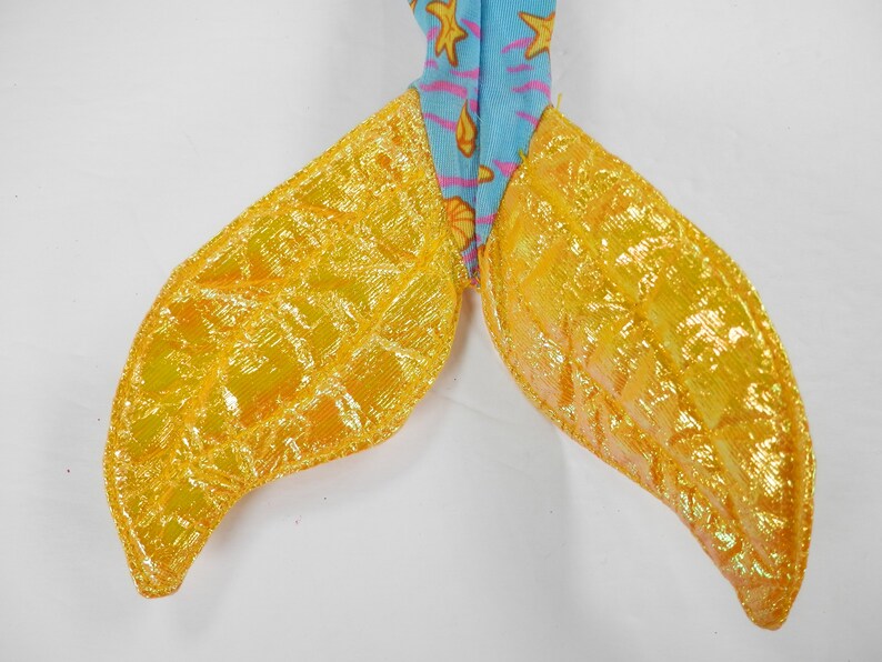 May include: A pair of yellow mermaid tail fins with a shimmery finish. The fins are made of fabric and have a textured surface.