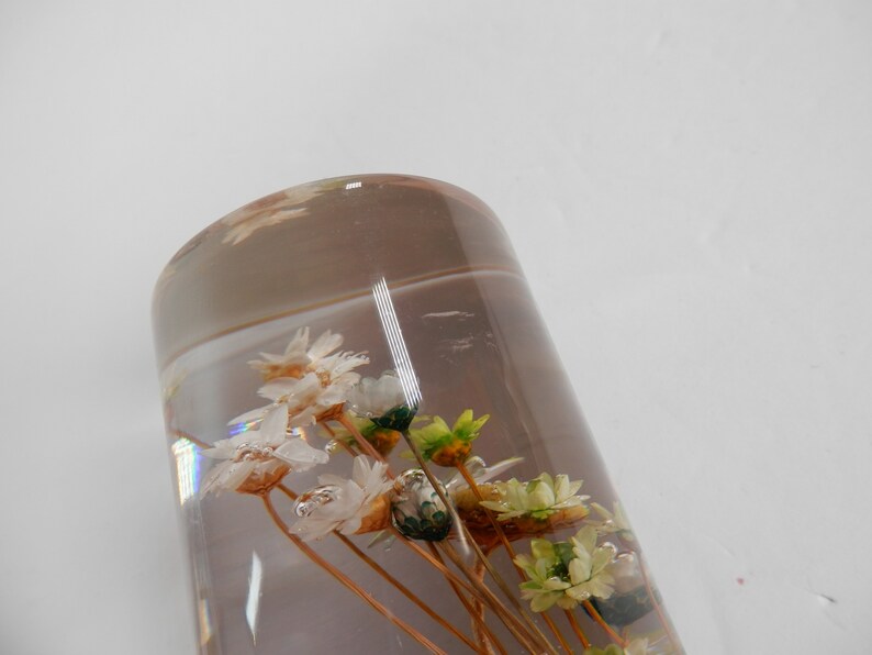May include: A clear glass cylinder filled with dried white and green flowers. The flowers are arranged in a bouquet and are suspended in the clear liquid.