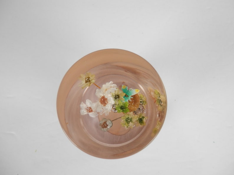May include: A clear glass bowl with a pink rim filled with dried flowers and leaves. The flowers are white and yellow, and the leaves are green.