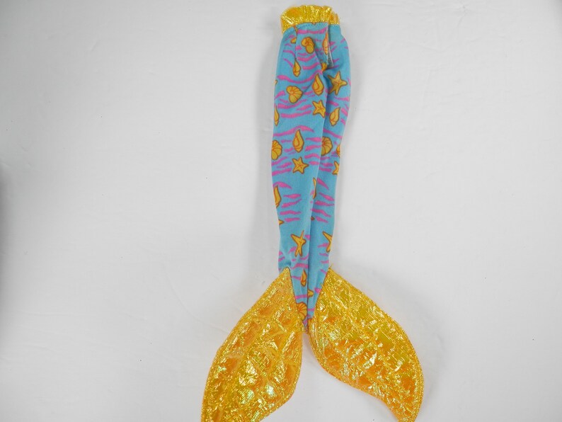 May include: A blue and yellow mermaid tail with a pink and yellow seashell pattern. The tail is made of fabric and has a shiny gold finish.