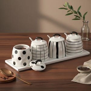 May include: A white ceramic spice jar set with black accents. The set includes jars with polka dots, grid, vertical stripes, and horizontal stripes. Each jar has a lid and a small spoon. The jars sit on a white rectangular tray.