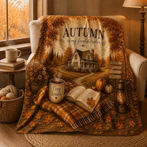 May include: A plush throw blanket featuring an autumn landscape with a house, a path, pumpkins, and a lantern. The text reads AUTUMN is my favorite color and Cozy Season. A mug and an open book are depicted on a plaid section of the blanket.