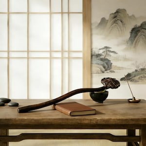 May include: A wooden table displays a brown notebook, a dark wooden incense holder with a flower-shaped end, a small green bowl, and a brass incense holder. The background features a traditional Asian-style painting.