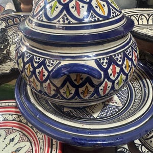 Peut inclure: Un tajine en céramique bleu et blanc avec un couvercle assorti, orné d'un motif géométrique détaillé avec des accents rouges, jaunes et verts. Le tajine repose sur un plat de service assorti, mettant en valeur l'artisanat marocain traditionnel.