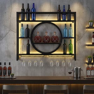 Puede incluir: Un botellero de metal negro con iluminación integrada exhibe varias botellas y copas de vino. El botellero tiene un estante circular y varios estantes rectangulares, con una barra y sillas en primer plano. La pared es de hormigón.