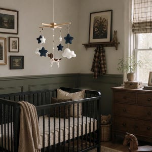 May include: A nursery mobile featuring a wooden cross frame with hanging felt elements including navy blue and white stars, white clouds, and a brown and white spotted dog figure, all suspended by white strings from a central point.