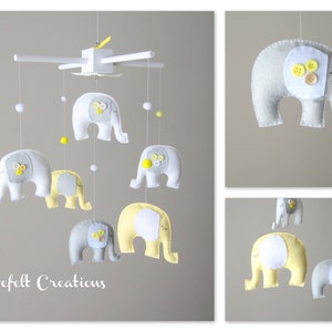 May include: A baby mobile with six grey and yellow felt elephants hanging from a white wooden frame. The elephants have white button eyes and yellow button accents.