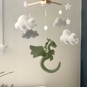 May include: A wooden mobile with a green felt dragon, white felt clouds, and white felt stars hanging from it.