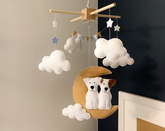 May include: A wooden mobile with white clouds, stars, and a crescent moon with two white dogs sitting on it. The mobile is hanging from a white ceiling.