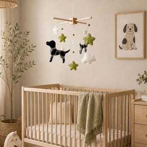 May include: A wooden baby mobile featuring hanging felt shapes including black and white spotted dogs, olive green stars, white stars, and white clouds suspended from a light wood cross frame with small wooden beads on white strings.