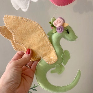 May include: A green felt dragon with yellow felt wings and a flower crown. The dragon is curled up with its tail in its mouth.