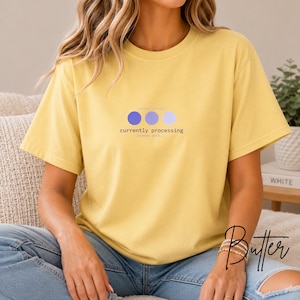 May include: A yellow short-sleeved t-shirt featuring a graphic design with three circles in shades of blue and purple. Below the circles, the text reads currently processing, with the smaller text please wait above and below the circles.