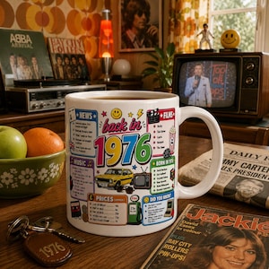 May include: A white ceramic mug featuring a colourful graphic design titled back in 1976. The print includes text about news, music, films, and prices from that year, alongside illustrations of a yellow car, a television, and a smiley face icon.