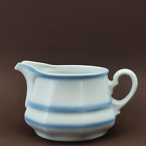 Könnte beinhalten: Weißer Keramik-Sahnegießer mit hellblauem Rand und zwei horizontalen blauen Streifen. Der Sahnegießer hat einen Ausguss und einen Griff. Der Sahnegießer hat ein klassisches Design, ideal zum Servieren von Sahne oder Milch.