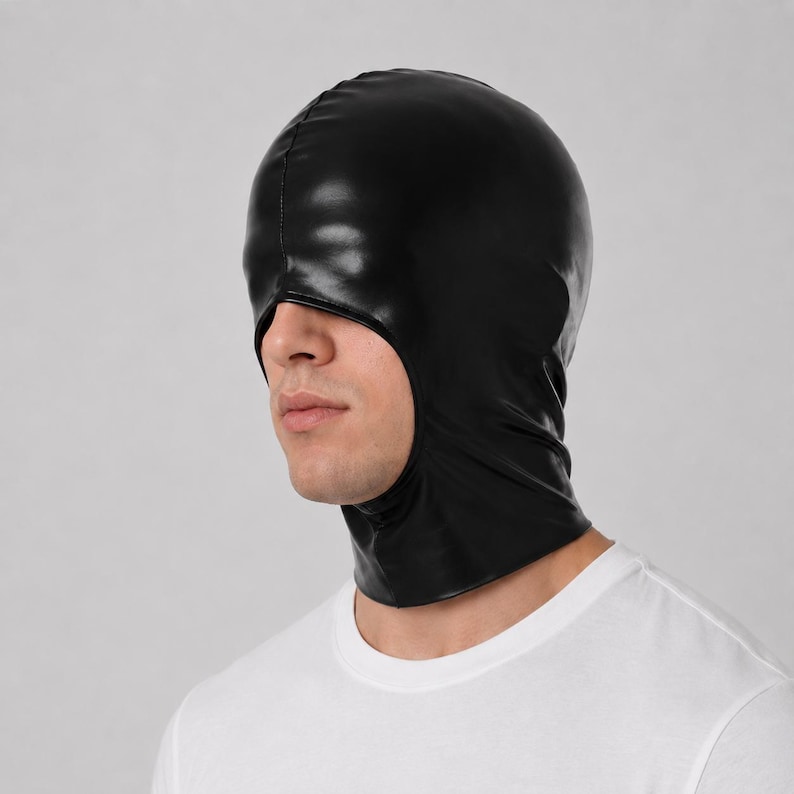 May include: A black hood made of a smooth, synthetic material with a glossy finish. The hood covers the entire head and neck, featuring a single large opening for the eyes, nose, and mouth area, with a vertical seam running down the center front.