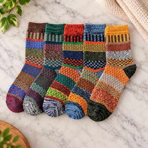 Op de afbeelding: Vijf sokken naast elkaar geplaatst, elk met een unieke combinatie van horizontale banden met ingewikkelde geometrische, geblokte en zigzagpatronen in levendige kleuren, waaronder bruin, groen, rood, blauw, oranje en geel.