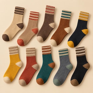 May include: A collection of ten crew socks arranged in two rows. Each sock features a solid color body, a contrasting ribbed cuff with horizontal stripes, and a distinctively colored heel and toe section in various earth tones and neutrals.