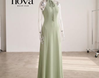 May include: A floor-length sage green halter dress featuring a high neck with a tie closure and a fitted bodice that flares into a long skirt. The text "nova WEAR HUB" is printed in black in the upper left corner of the image.