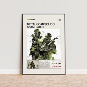 May include: A framed poster featuring the game "Metal Gear Solid 3: Snake Eater." The artwork depicts two characters in camouflage, holding weapons. The poster has a cream background with green and black accents, and the Konami logo.