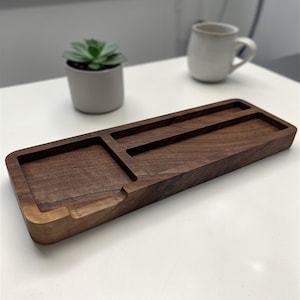May include: A rectangular wooden desk organizer with a dark brown finish. It features a square compartment, a long slot, and a smaller slot. The organizer is designed to hold office supplies and keep a desk tidy.